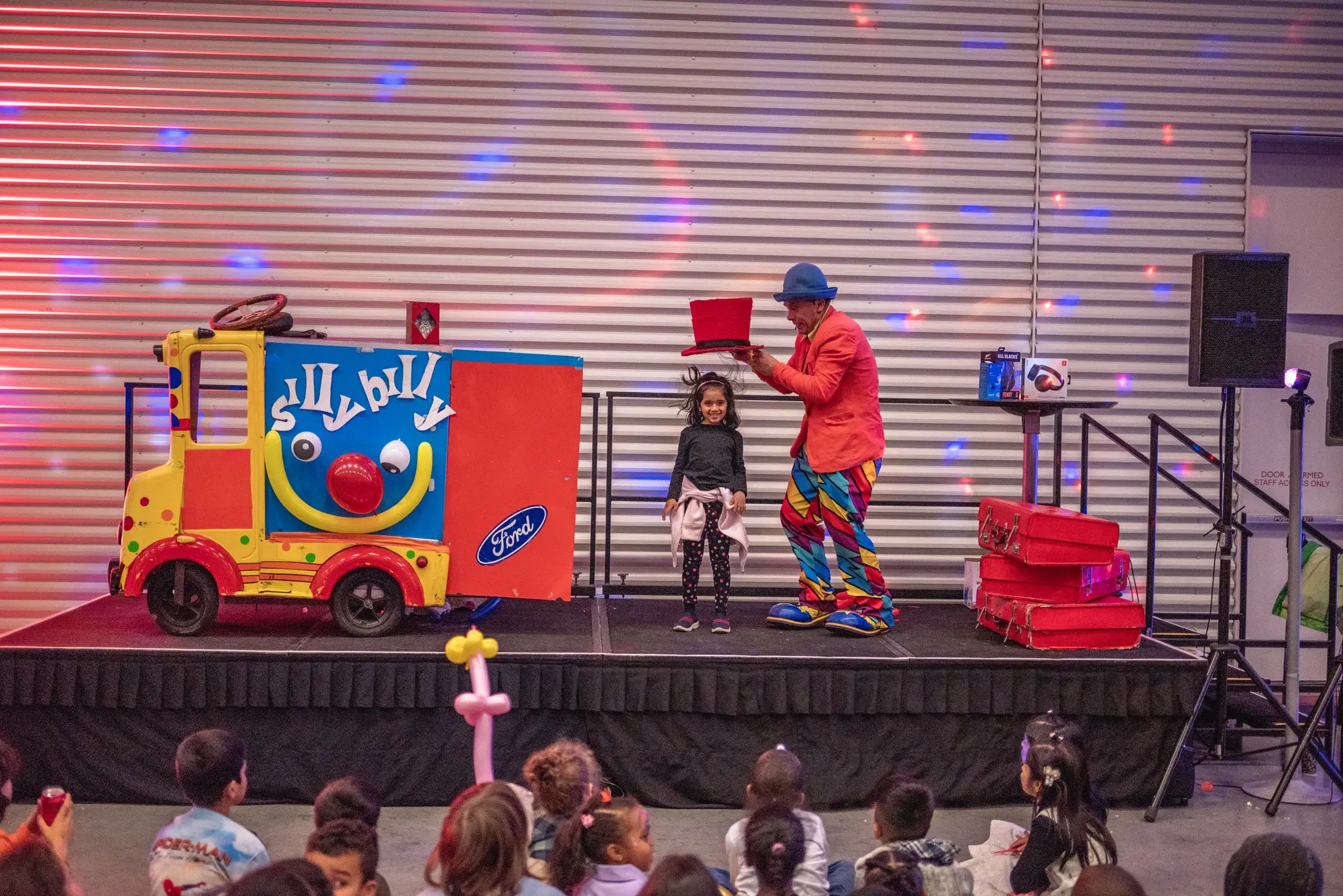 Silly Billy performing his Stage Magic Show with the iconic Betty Ford Clown Car backdrop and a young volunteer on stage